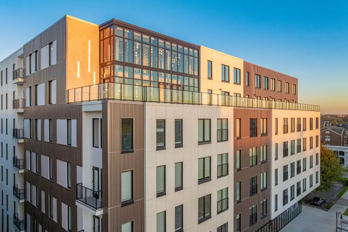 Modern rooftop view of a building with expansive glass windows reflecting sunset hues. The sleek design and railings convey a contemporary, serene atmosphere.