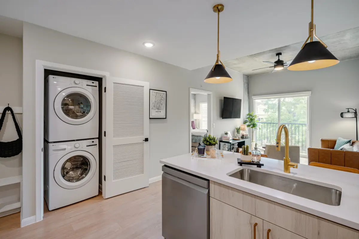 Modern open-concept living space with a sleek kitchen island and gold fixtures. A stackable washer and dryer are visible beside a cozy living area.