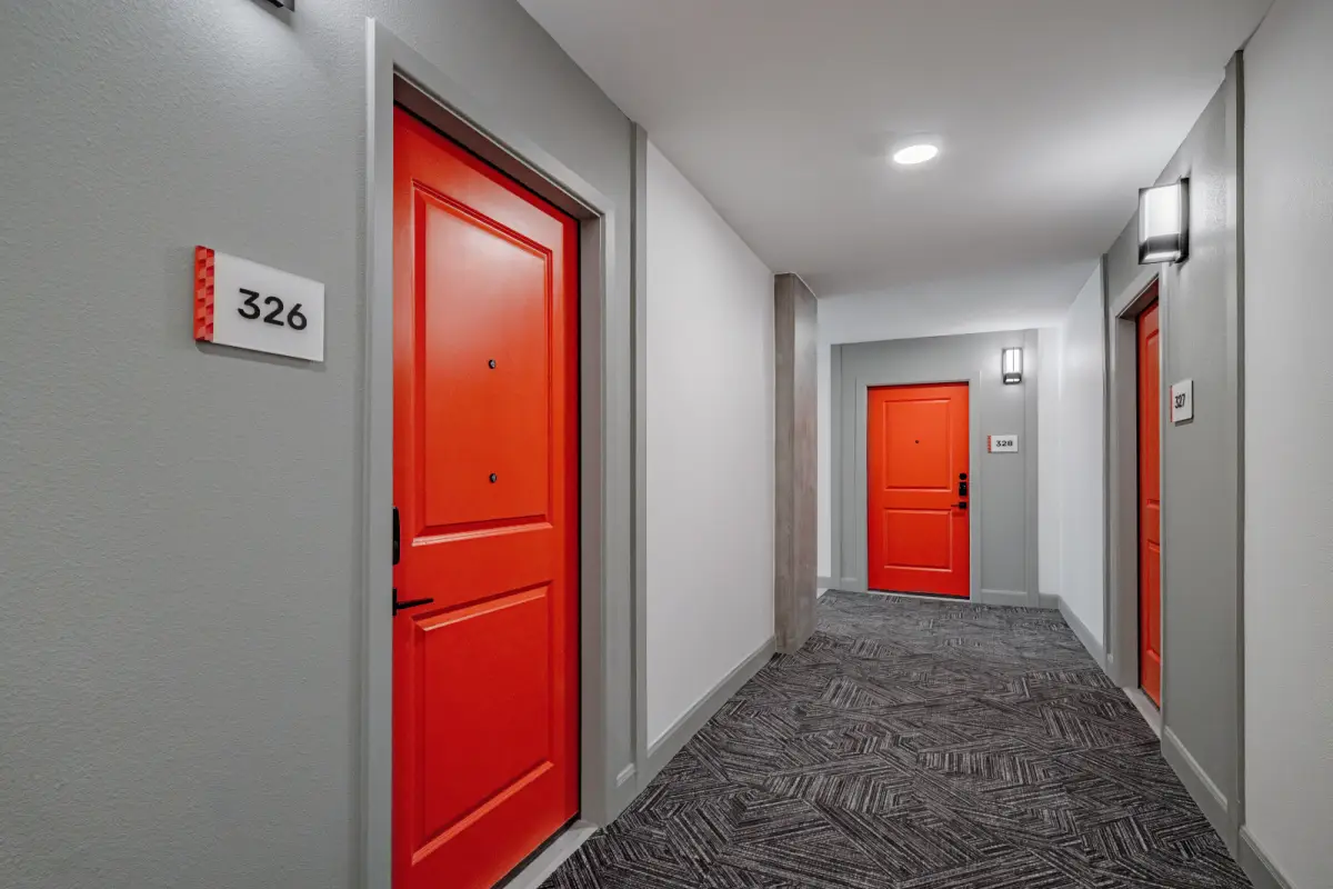 Hallway with gray walls and patterned carpet, featuring bold red doors numbered 326 and 317. Bright lighting creates a modern, inviting atmosphere.