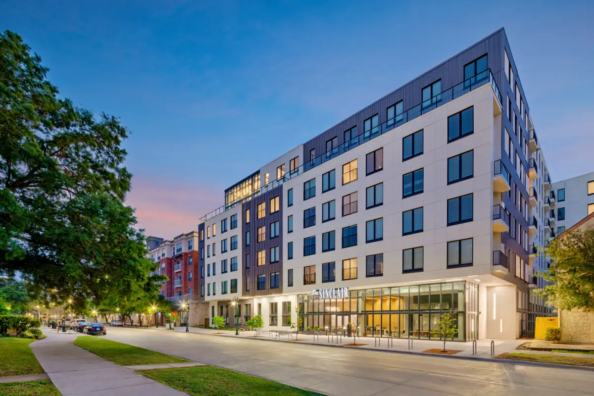 Modern six-story building with a mix of vertical panels and large windows under a blue sky. Street-level greenery and benches enhance the inviting atmosphere.
